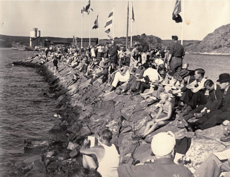Publik och flaggor på stenpir i Uddevallas yttre hamn.