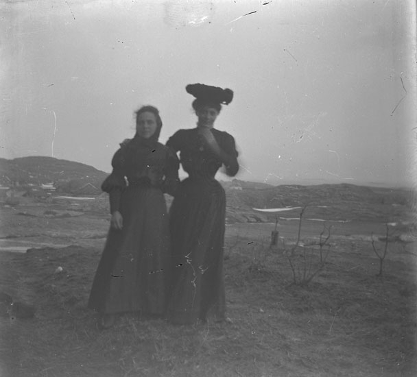 Två kvinnor ute o blåsten. En med hatt.