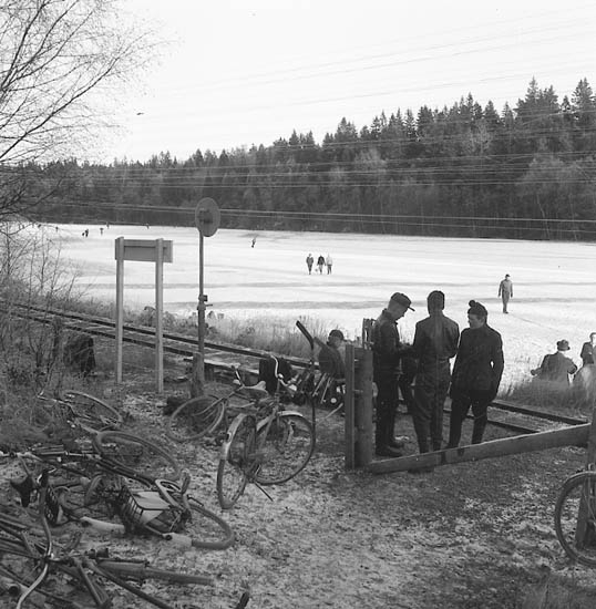 Bjursjön Uddevalla vintertid. Cyklar i förgrunden och skridskoåkare i bakgrunden. Lelångens järnväg (Lelångenbanan) skär genom bilden.