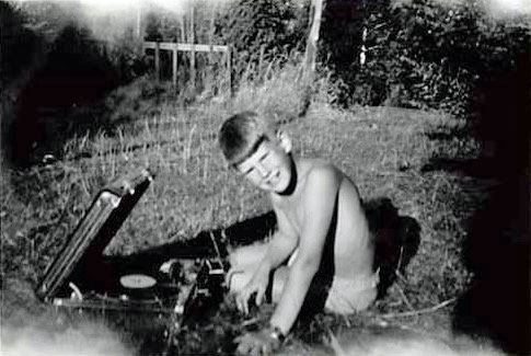 Yngre pojk sitter i gräset med en grammofon. Svartvit bild