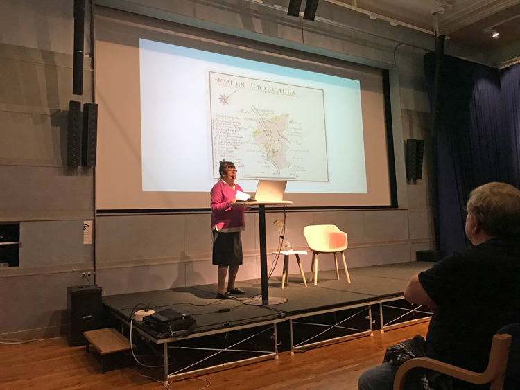 Maria Gustavsdotter som är författare håller föredrag om det Myrtengrenska mordet. På filmduken i bakgrunden syns en äldre karta över Uddevalla stad.