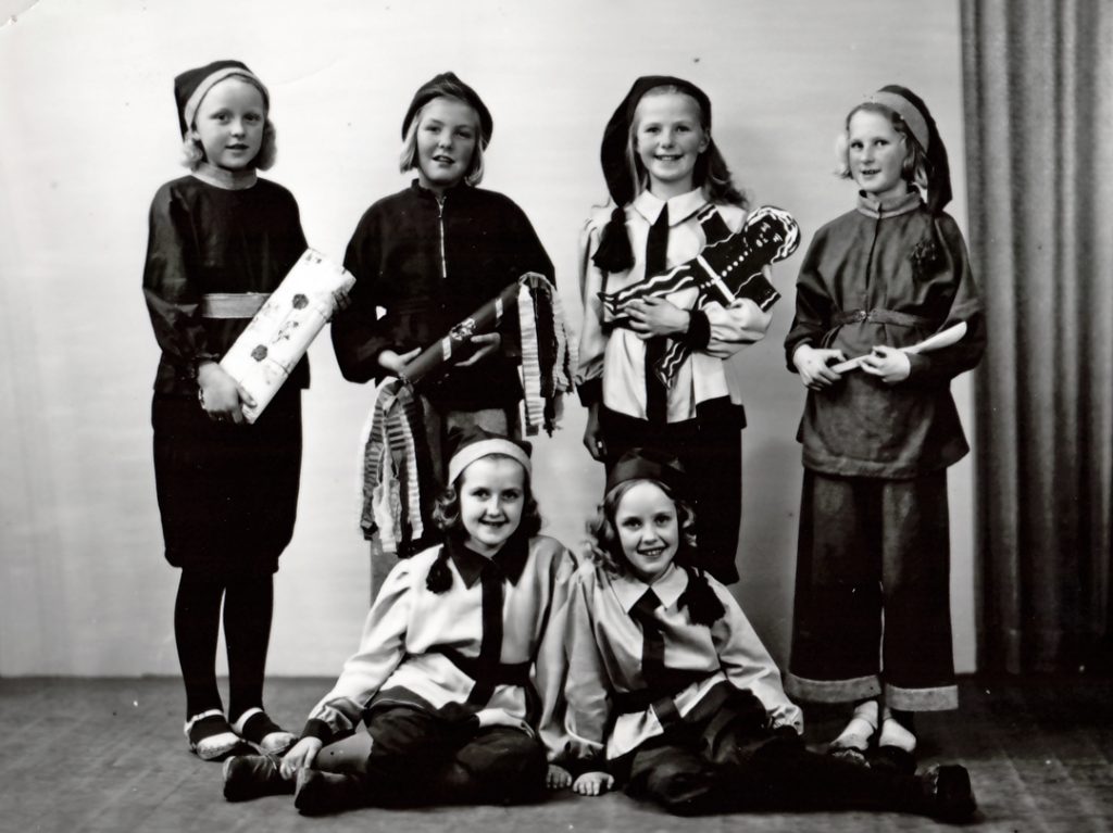 Äldre svartvitt foto förställande sex barn utklädda till tomtar. Några av barnen har paket i famnen.