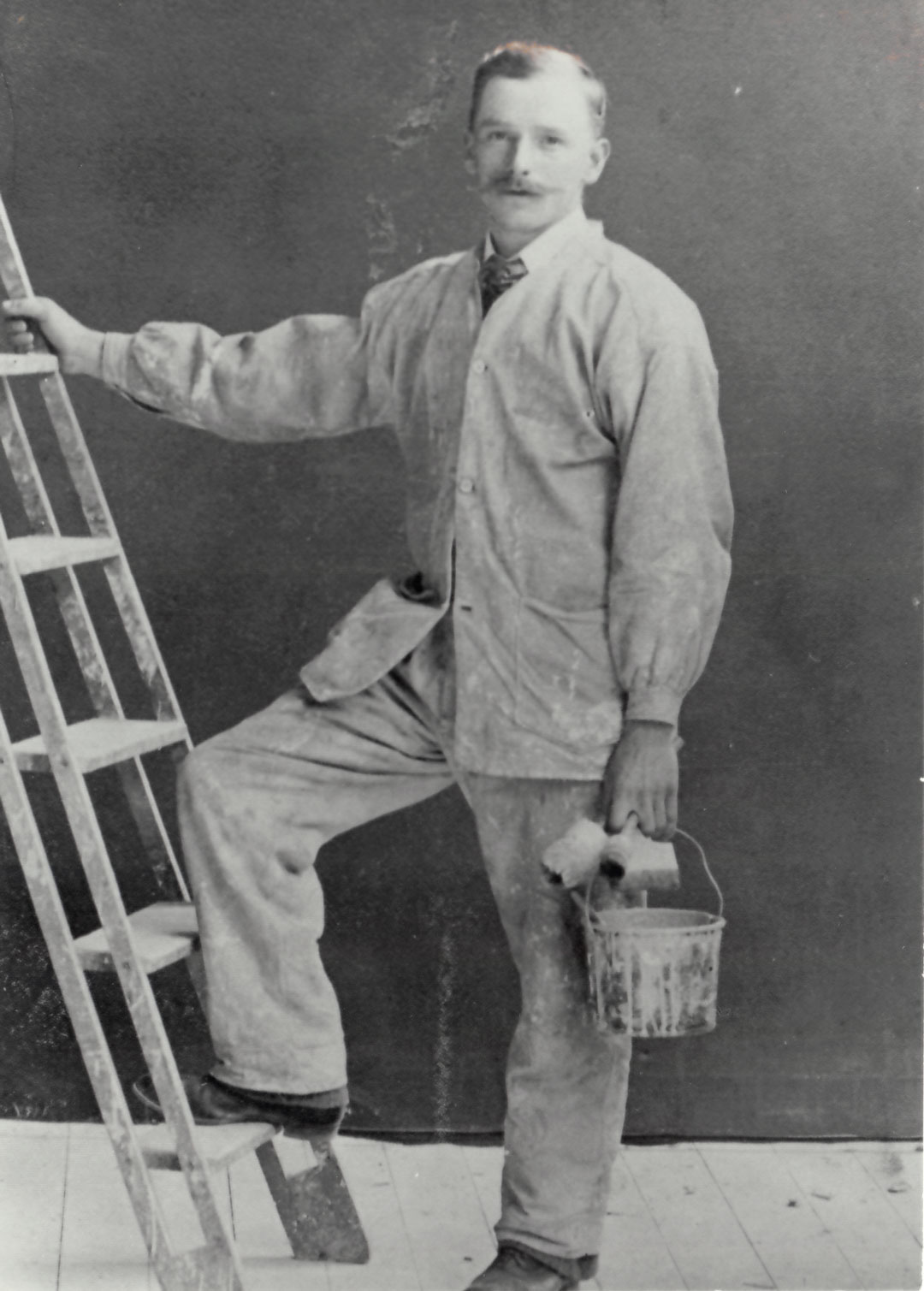 Ensam målare poserar med en fot och hand på en stege, i andra handen har han färgburk och penslar.