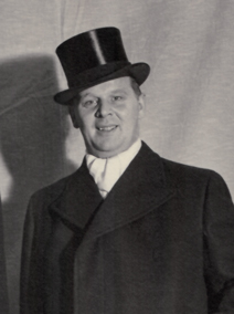 Porträtt av Einar Dahl. Einar har på sig cylinderhatt, vit halsduk och överrock. Bilden är svartvit.